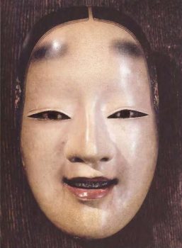 Besišypsančios moters ko-omote (Mažas veidas). Vienas iš dešimties japonų No teatro moterų kaukių tipų, kurias usidėdavo vyrai, vaidindami moteris. Kongo mokykla, Kioto prefektūra, Japonija. | Nuotr. iš kn. "The book of symbols".