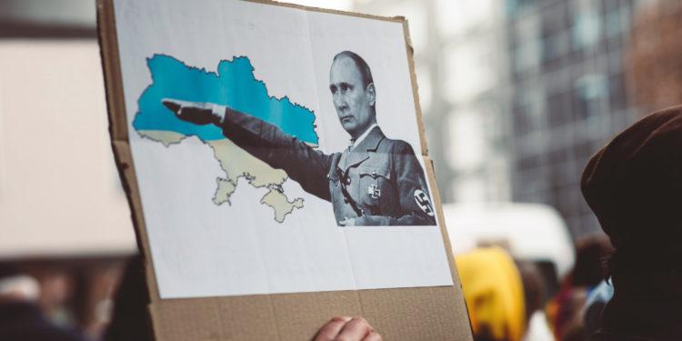 Mitinge žmonės laiko plakatą su hitleriškai besisveikinančio V. Putino atvaizdu