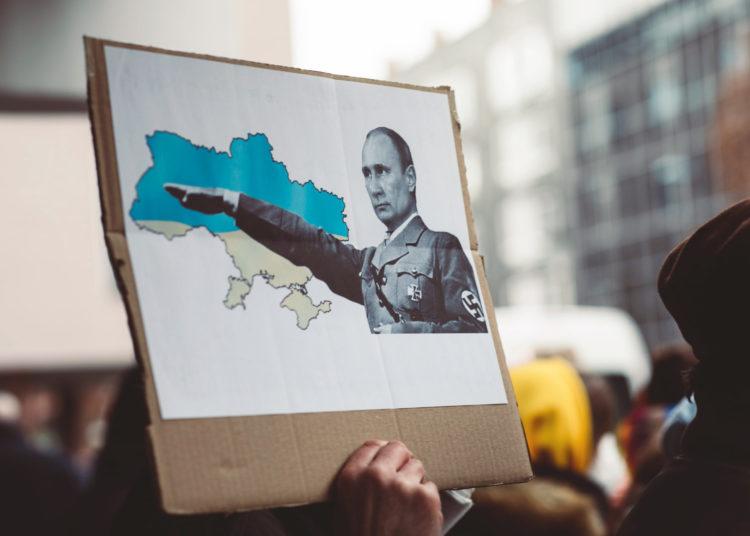 Mitinge žmonės laiko plakatą su hitleriškai besisveikinančio V. Putino atvaizdu