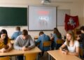 Tuščioje klasėje mokiniai spokso į telefonus, projektorius rodo serialo plakatą, o istorinė Vyties vėliava kabo sukritusi kampe – Žalgirio metinių pamiršimo metafora.