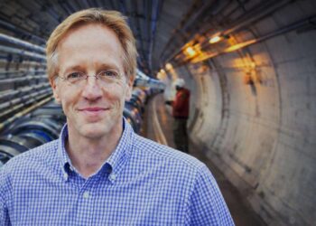 Robertas Deikgrafas o jam už nugaros dalelių greitintuvo tunelio siluetas