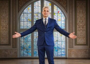 Rimantas Balsys išskiestomis rankomis Klaipėdos universiteto Vitražų menės fone