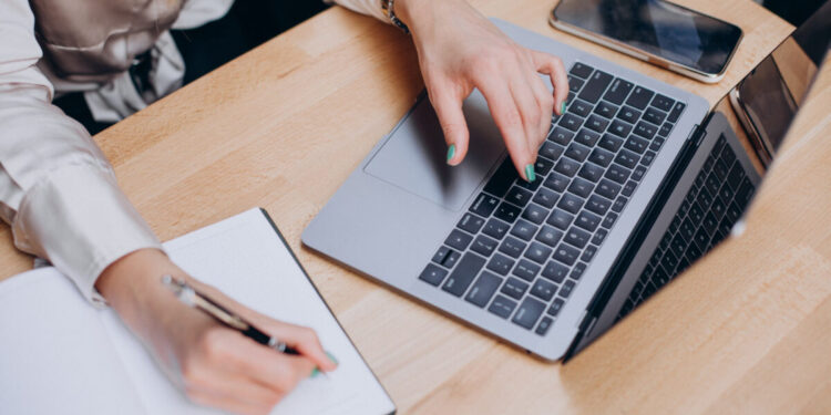 Nešiojamas kompiuteris, popieriaus lapas ir rašanti ranka