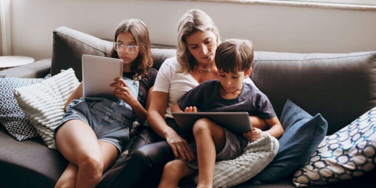Mama su vaikais sėdi ant sofos ir naudojasi 5g namų internetu