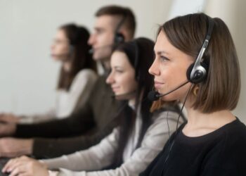 Telefonistės su ausinėmis prie kompiuterių