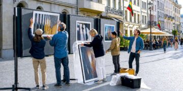 Žmonės miesto aikštėje rengia lauko fotografijų parodą