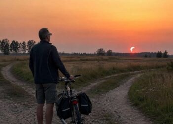 Žmogus su dviračiu ties lauko kelių išsišakojimu stebi dalinį Saulės užtemimą