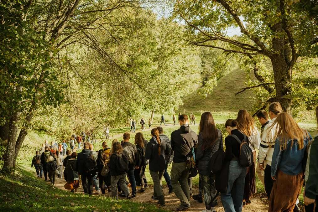 Gausus būrys žmonių leidžiasi taku tarp medžių Kernavėje