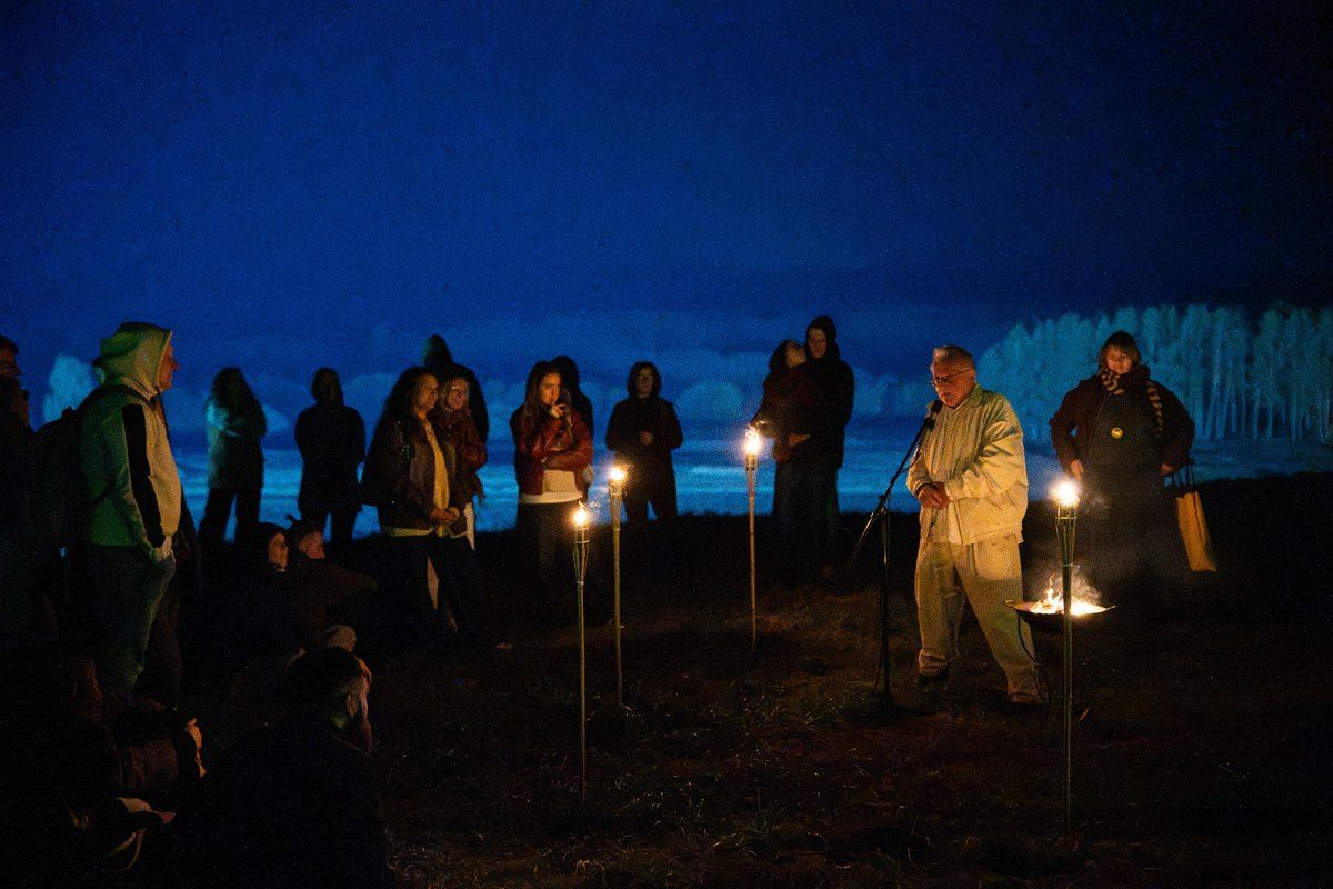 Vyras kalba prie mikrofono naktį, aplink jį dega deglai ir matyti apšviestas Kernavės kraštovaizdis