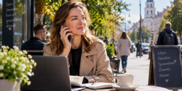 Moteris saulėtą rugsėjo dieną kalbasi telefonu miesto kavinėje