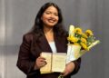 Astrofizikė Barkha Yakub Bale su daktaro diplomu ir geltonų gėlių puokšte