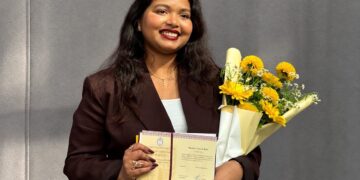 Astrofizikė Barkha Yakub Bale su daktaro diplomu ir geltonų gėlių puokšte