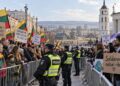 Dvi mitinguotojų grupės su Lietuvos vėliavomis ir migracijos politikos plakatais, atskirtos policijos užtvaromis