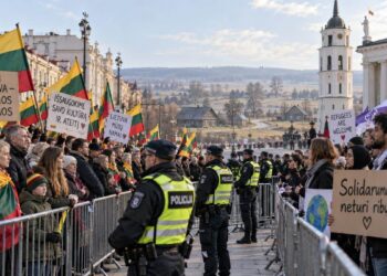 Dvi mitinguotojų grupės su Lietuvos vėliavomis ir migracijos politikos plakatais, atskirtos policijos užtvaromis