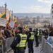 Dvi mitinguotojų grupės su Lietuvos vėliavomis ir migracijos politikos plakatais, atskirtos policijos užtvaromis
