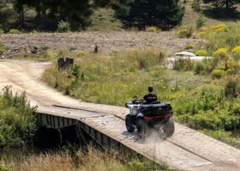 Keturratis su vairuotoju važiuoja per medinį tiltą gamtoje