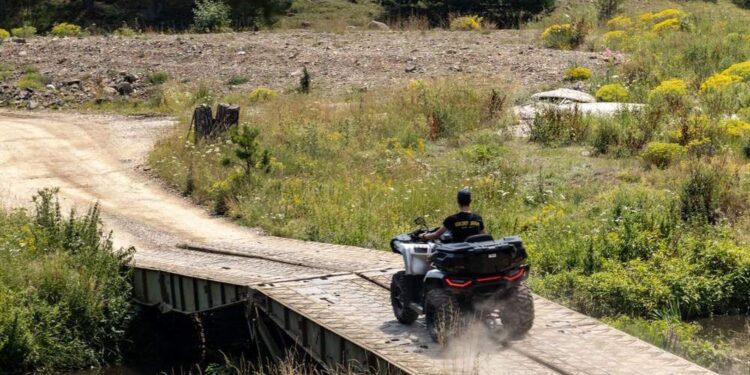 Keturratis su vairuotoju važiuoja per medinį tiltą gamtoje