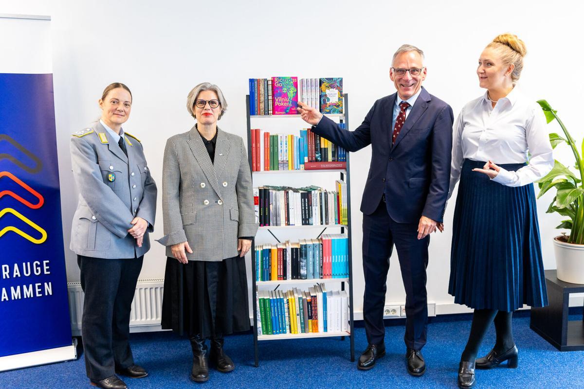 Renginio dalyviai prie lietuvių autorių knygų lentynos.