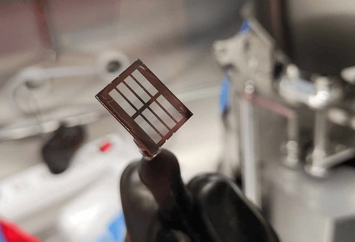 Laboratorijoje laikomas plonas perovskitinis saulės elementas su matomomis šviesą sugeriančiomis juostelėmis