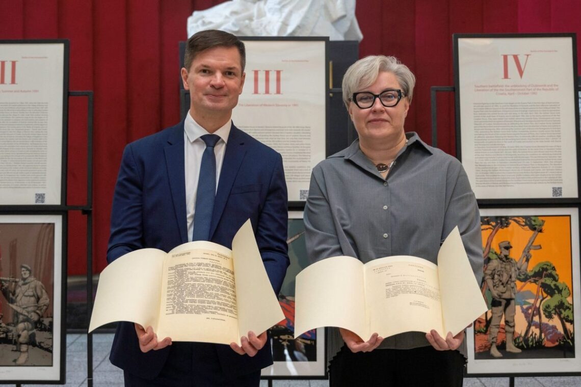 P. Saudargas ir muziejaus atstovė laiko Lietuvos Vietinės rinktinės dokumentus