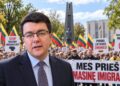 Vytautas Sinica protesto prieš masinę imigraciją fone