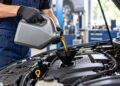 Autoserviso darbuotojas pila variklio alyvą per piltuvą į automobilio variklį