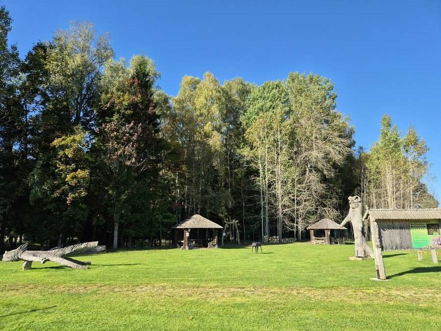 Žalia stovyklavietės pieva su medinėmis pavėsinėmis